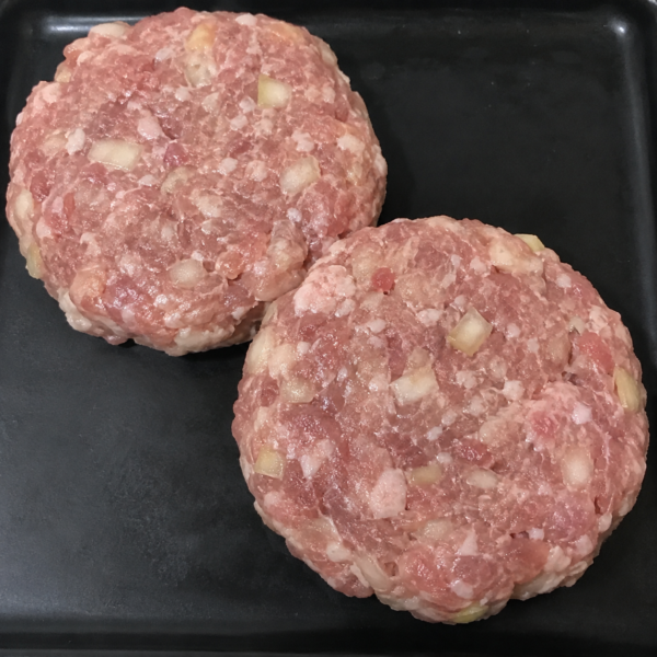Illustrative image of raw pork and apple burgers on a black butcher’s tray